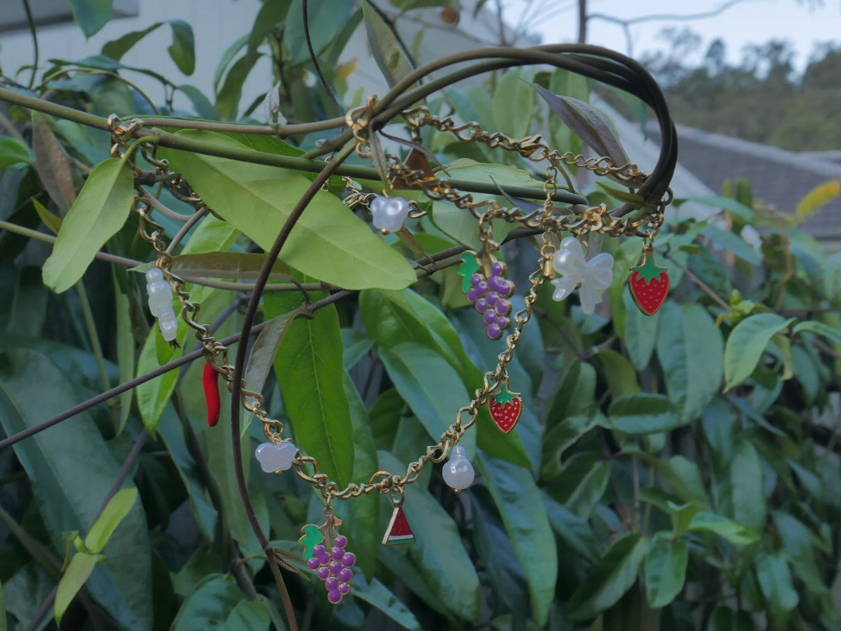 Bracelet with grape charms hanging on a branch with green leaves in the background