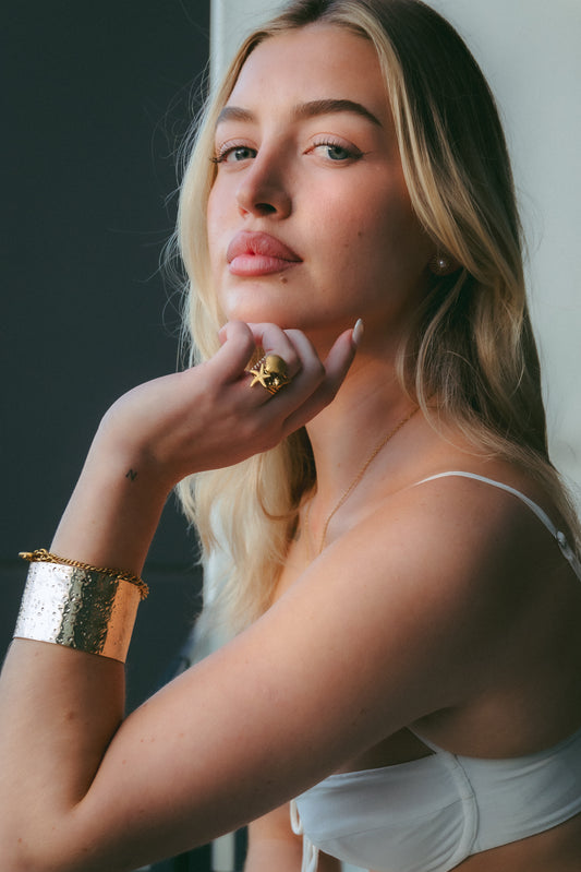 Woman wearing a white top with gold r jewelry against a neutral background