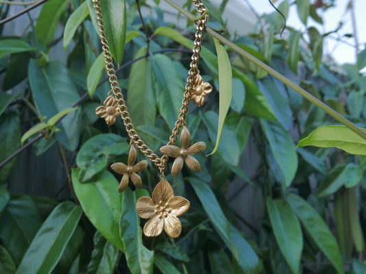 Gold floral necklace against a green leafy background