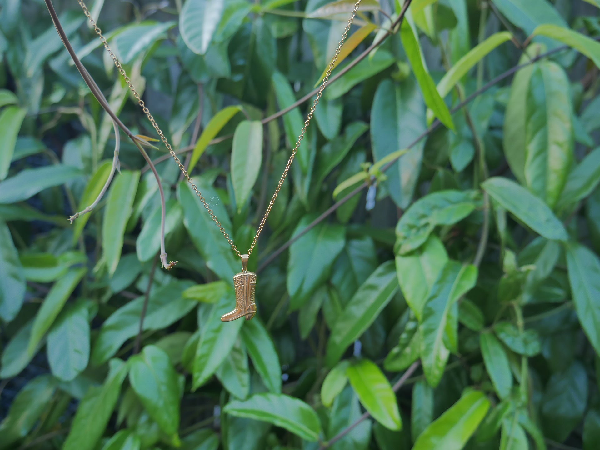 Gold necklace with a pendant on a green leafy background