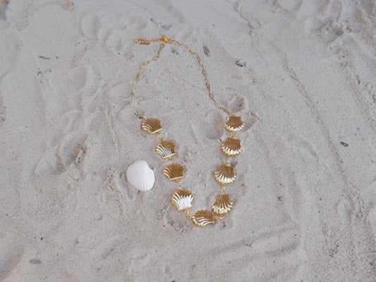 Gold shell necklace and bracelet on sandy surface
