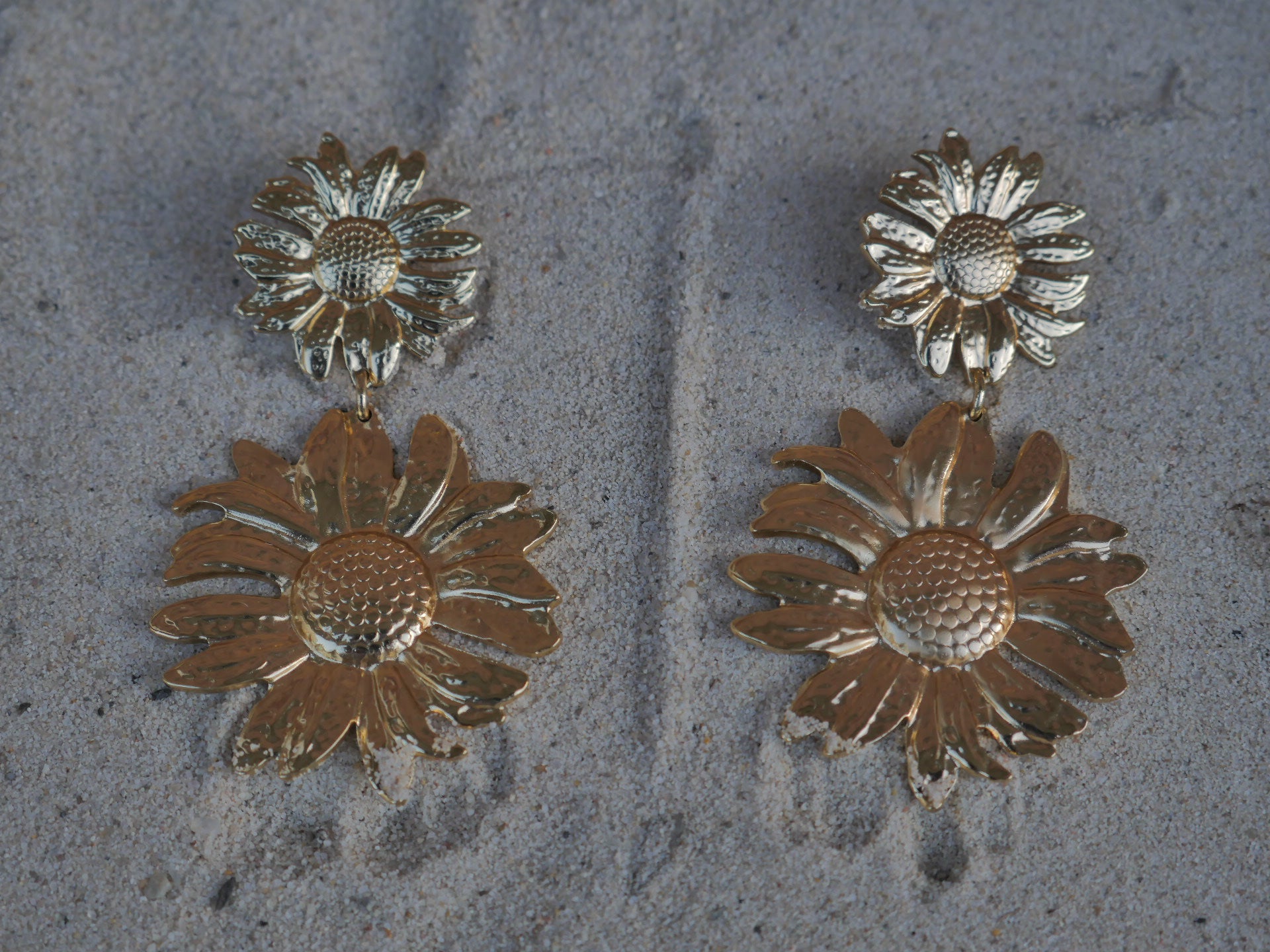 Gold sunflower-shaped earrings on a textured surface