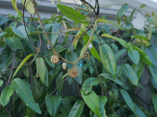 Gold necklace with charms hanging among green leaves