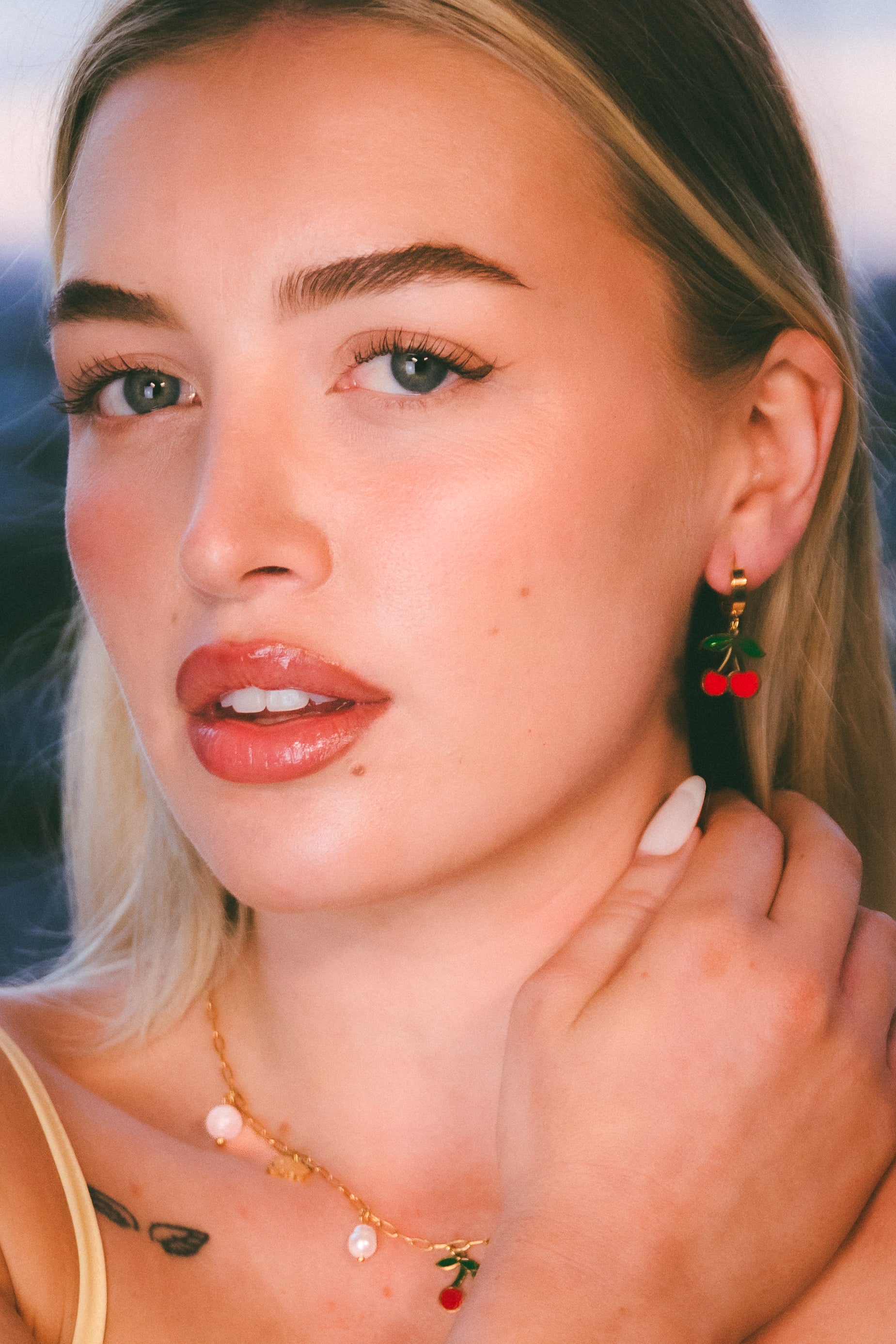 Close-up of a woman wearing earrings with red cherries against a blurred natural background