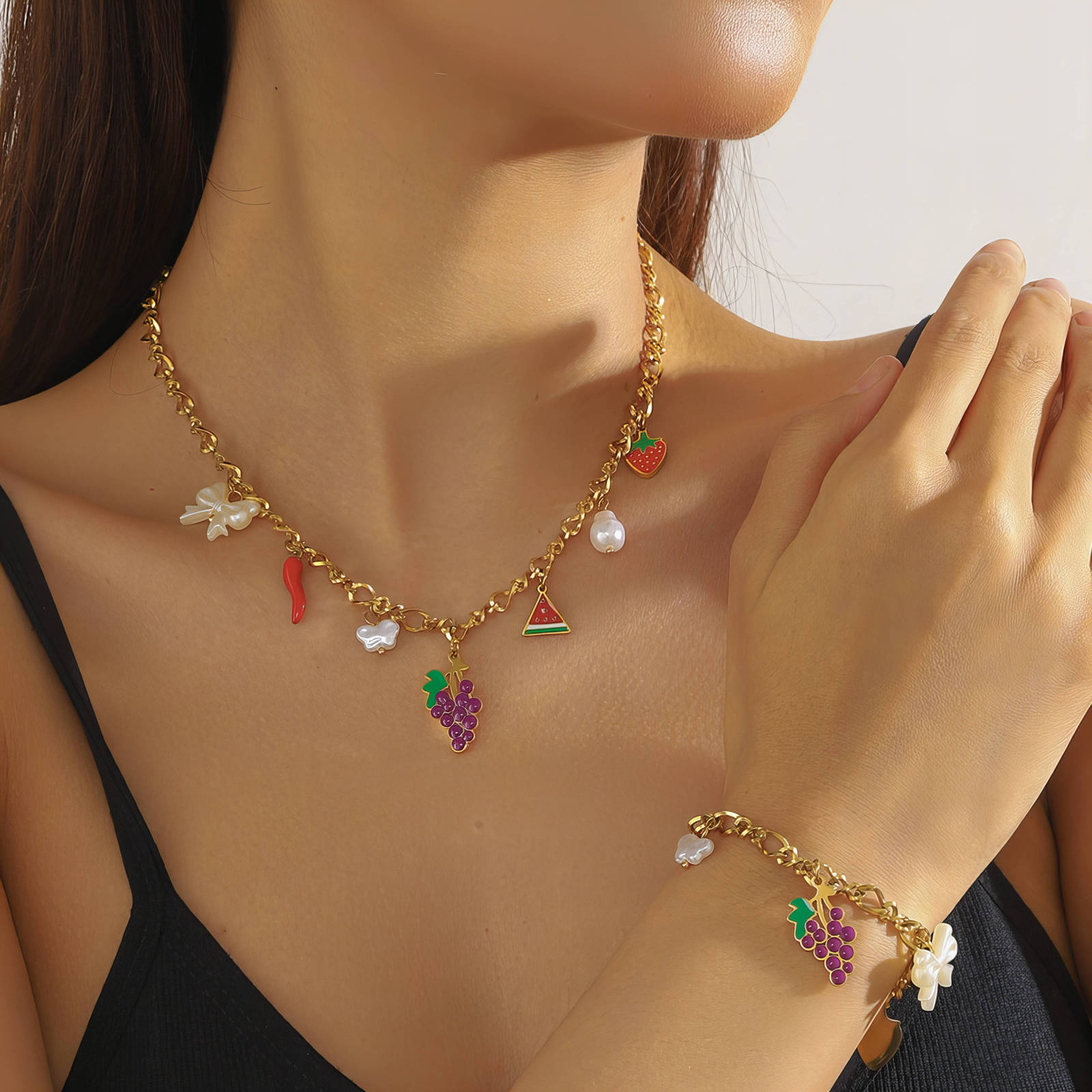 Woman wearing a gold necklace and bracelet with colorful charms on a neutral background