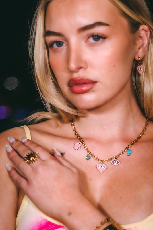 Close-up of a person wearing a necklace with colorful charms and a ring on a dark background