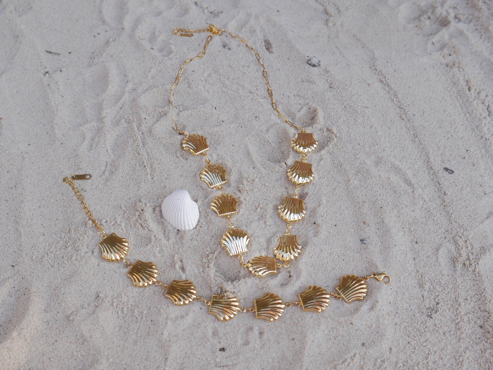 Gold shell necklace and bracelet on sandy surface