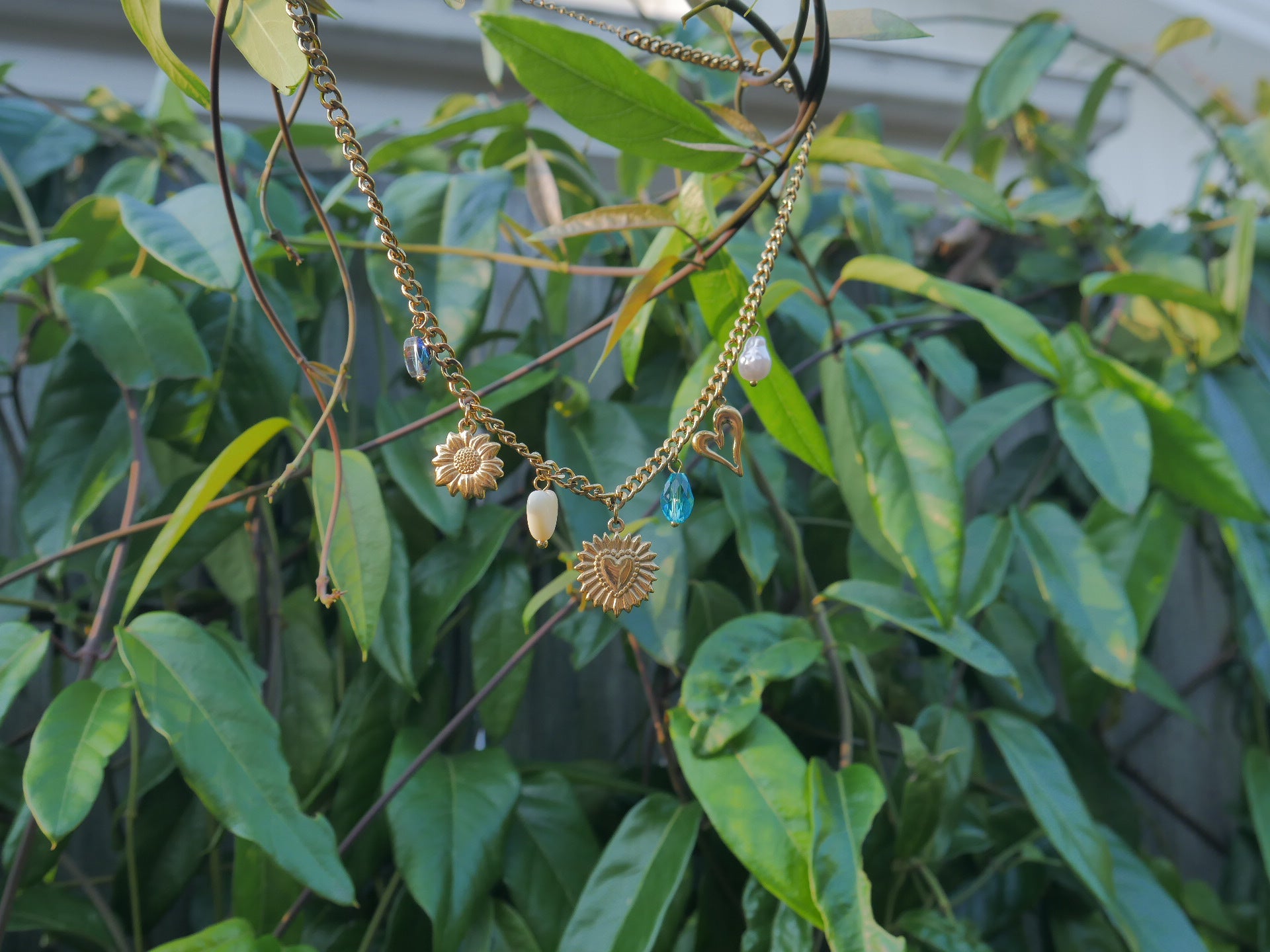 Necklace with gold pendants and charms hanging among green leaves