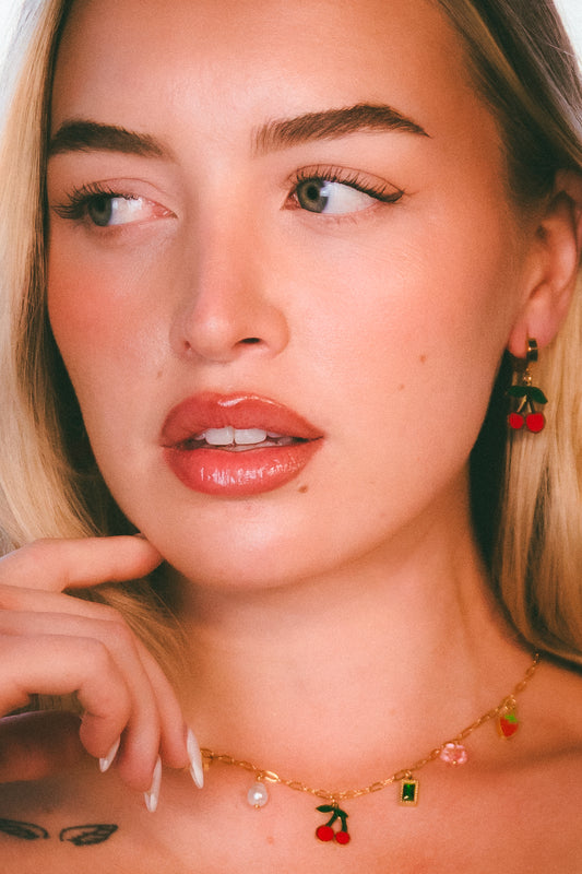 Close-up of a woman wearing a gold necklace with cherry pendants.

