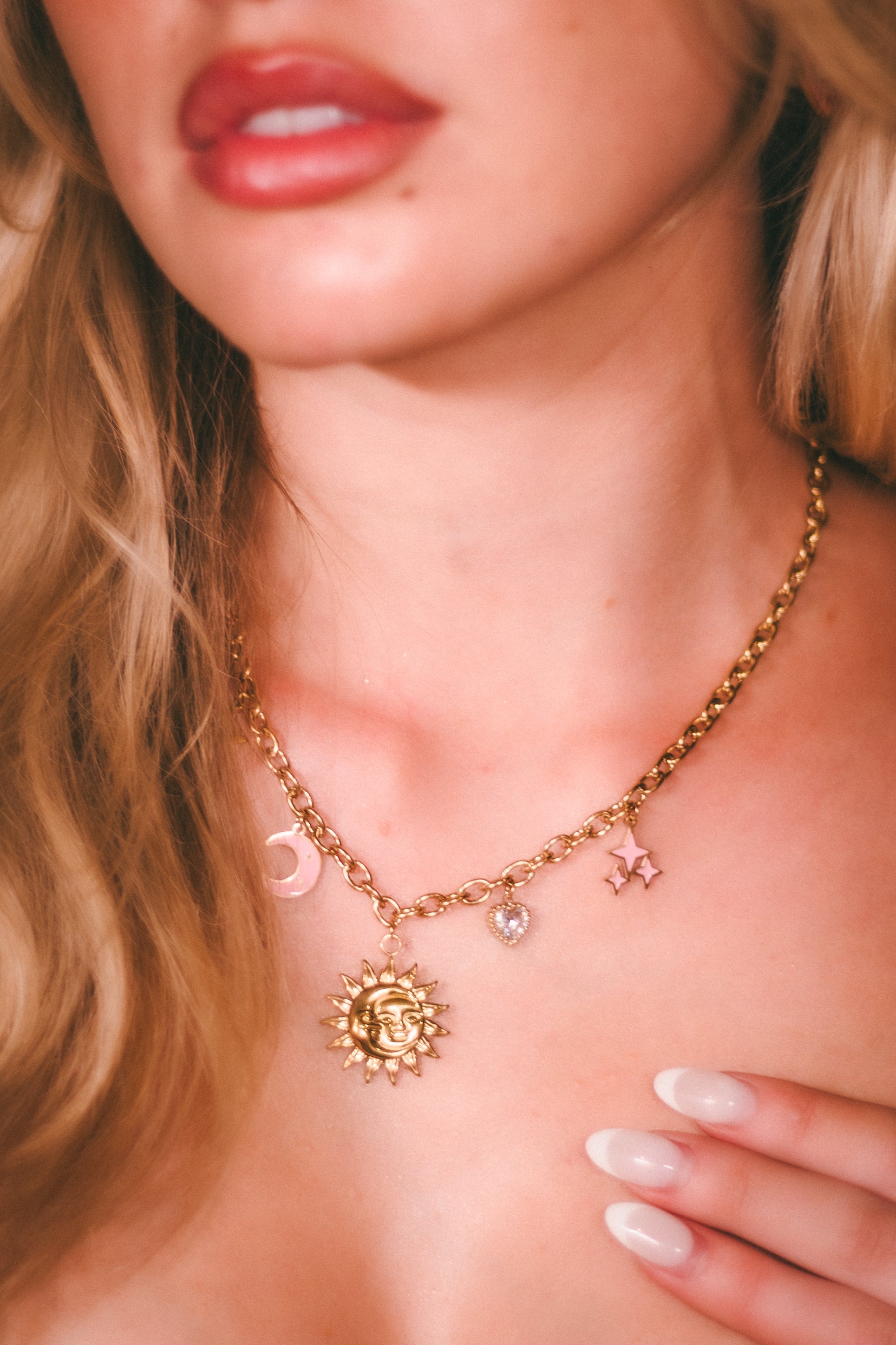 Close-up of a woman wearing a gold necklace with charms, focusing on the neck and upper chest area.