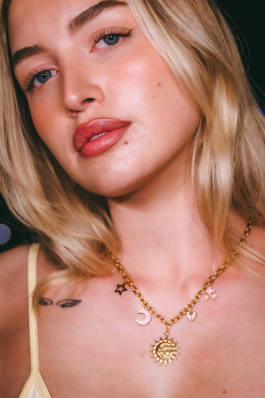 Close-up of a person wearing a gold necklace with various pendants.