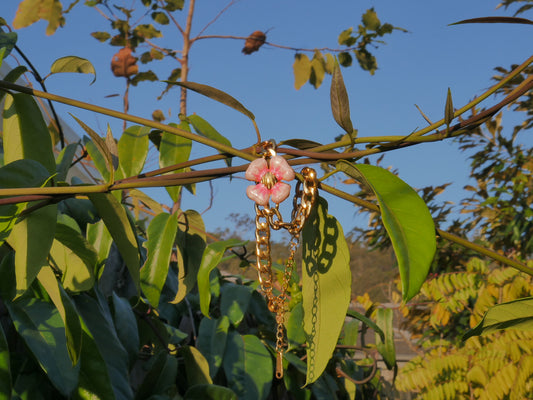 Gold chain with a pink flower charm hanging among green leaves