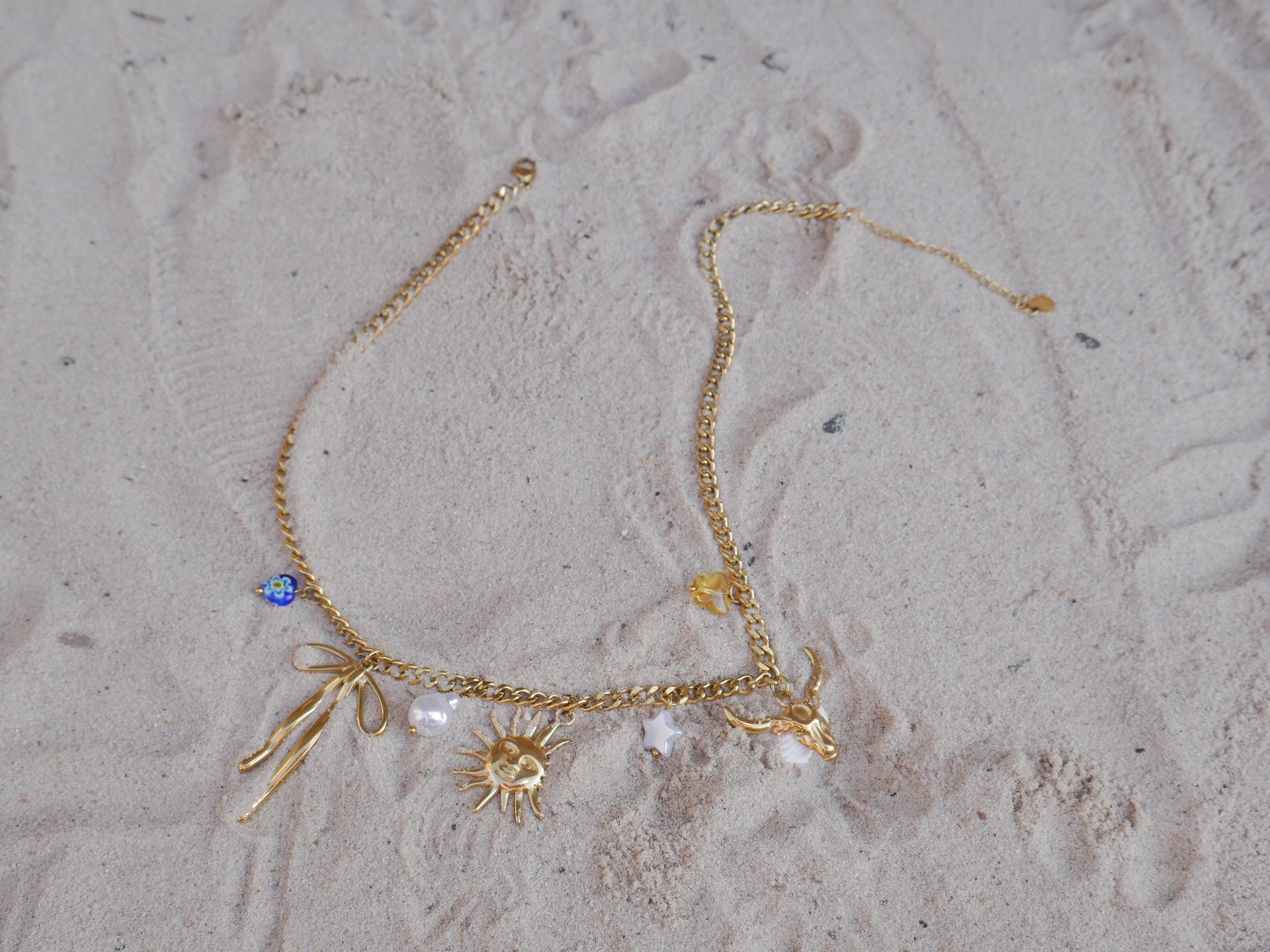 Gold necklace with charms on a textured beige surface