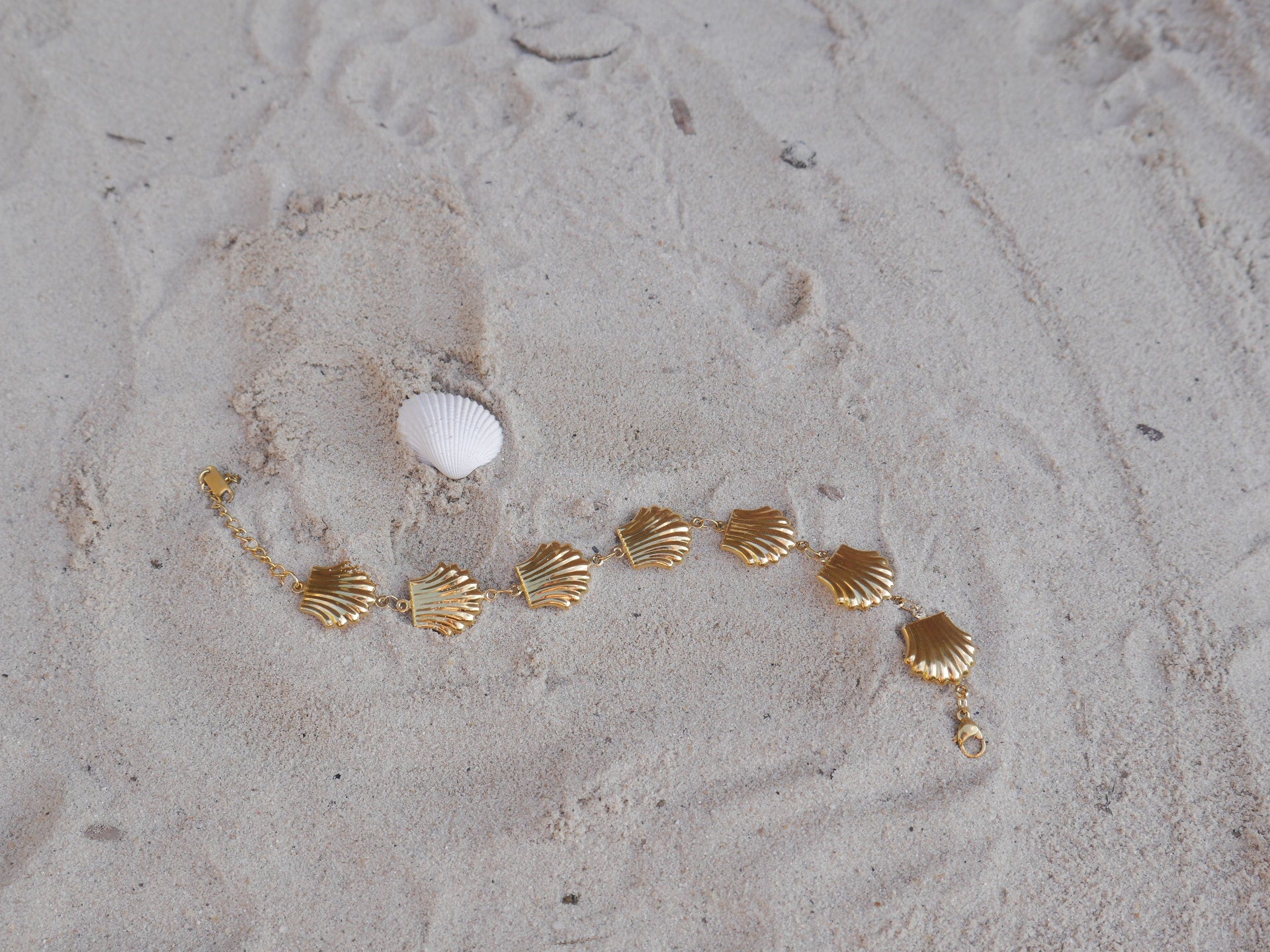 Gold bracelet with shell-like charms on a sandy surface